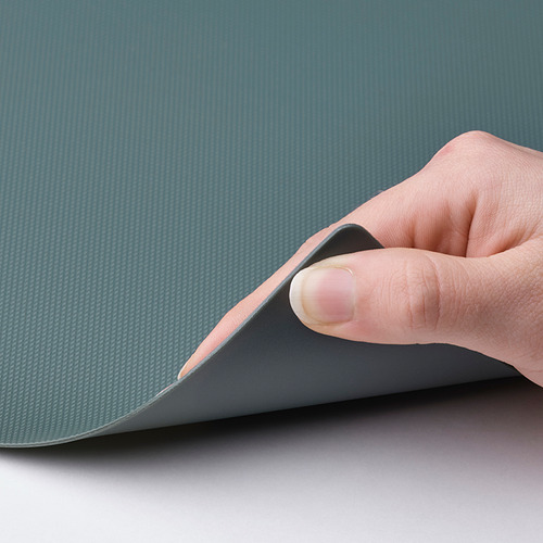 Una mano retira una tabla de cortar FINFÖRDELA azul y flexible, dejando al descubierto su parte inferior texturizada.