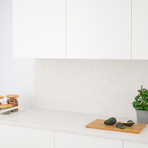 Cocina moderna con encimera de cuarzo blanco y placa para salpicaduras, que muestra aguacates y plantas en una tabla de cortar de madera.