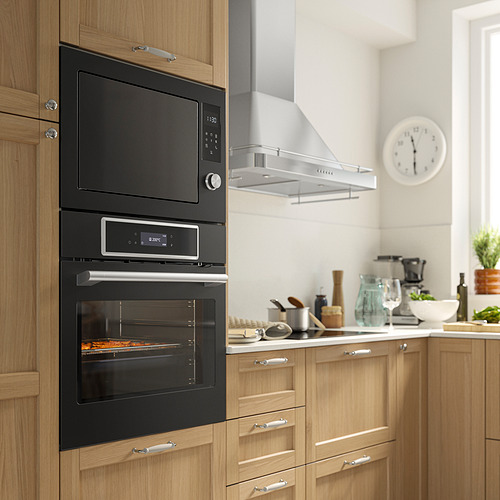 Cocina moderna con horno IKEA STENABY negro, microondas empotrado, armarios de madera y varios electrodomésticos y utensilios de encimera.