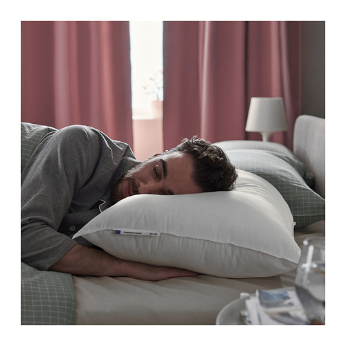 La persona duerme plácidamente sobre una almohada blanca SMÅSPORRE , sudadera gris, cama con cortinas rojas.