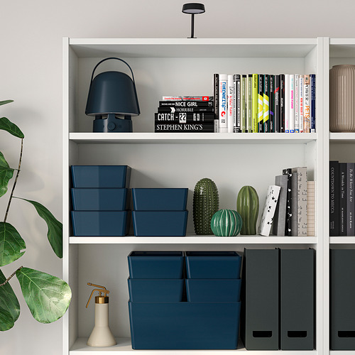 Estantería blanca con cajas azules, plantas verdes y una lámpara azul.