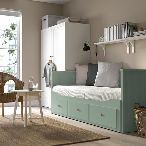 Pequeño dormitorio moderno con sofá cama verde HEMNES, armario blanco y mesa redonda. Decoración acogedora y minimalista con iluminación tenue.