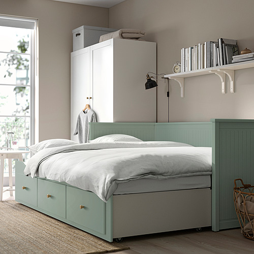 Sofá cama HEMNES con cajones, almohadas blancas. Armario blanco con libros, lámpara y ventana.