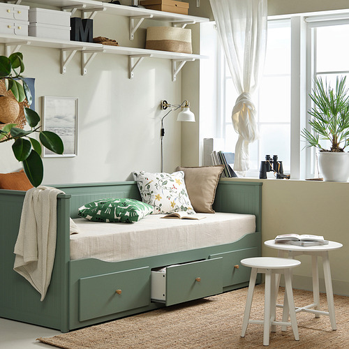 Sofá cama HEMNES de color verde grisáceo con almacenaje, se convierte de sofá a cama doble. Robusta estructura lacada, cojines y dos taburetes. La planta de interior añade naturaleza.