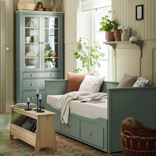 Sofá cama HEMNES en verde grisáceo, estilo sofá, junto a la ventana junto a los armarios y un acogedor rincón con manta y libros.