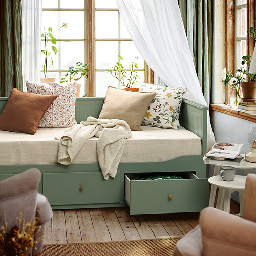 Sofá cama HEMNES en color verde grisáceo, sofá/cama con almacenaje, almohadas, manta, planta, taza.