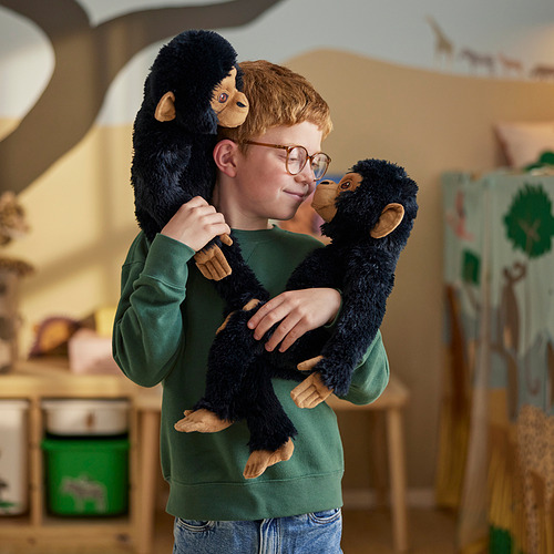 Un niño abraza a dos chimpancés de peluche en una habitación acogedora. Los chimpancés tienen sujetadores de contacto y cierre en las manos y los pies, lo que les permite aferrarse.
