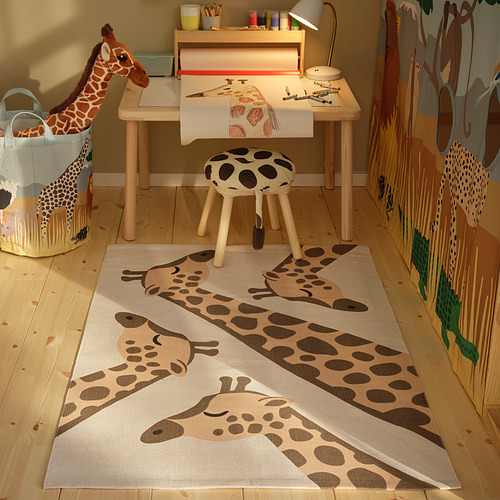 Alfombra de jirafa SANDLÖPARE sobre suelo de madera, con mesa, taburete y cesta de juguetes.