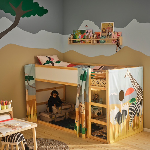 Cama KURA con cortina de temática safari, con diseño de jirafa, árbol y sabana, erguida en una habitación para niños, rodeada de muebles más pequeños.