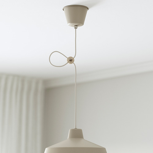 Una lámpara colgante de color beige cuelga del techo con un cordón ajustable, proporcionando luz dirigida.
