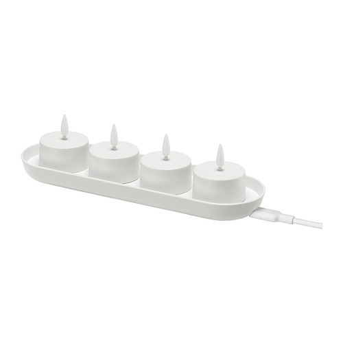 Imagen Candeleros led SKATGÅS, blancos, en una bandeja de carga. Cuatro velas cilíndricas con puntas en forma de llama, conectadas por un cable blanco.