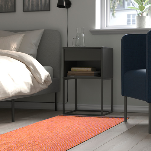 Dormitorio moderno con una cama gris, mesita de noche negra con libros y una alfombra colorida, que agrega calidez y textura a la habitación.