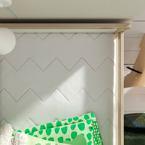 Una cama para niños con una pared con patrón de zigzag detrás, con un colchón de lunares verdes.