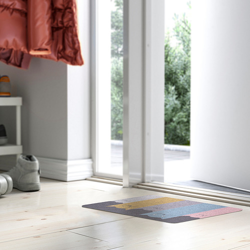 Felpudo colorido de TURISTVÄG en suelo blanco cerca de zapatos grises y gran ventanal.