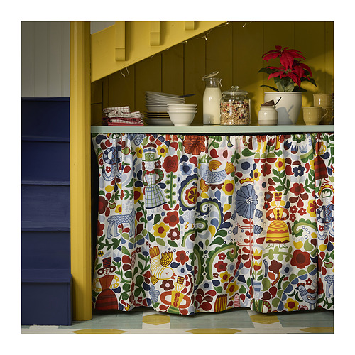 Cocina luminosa con cortina floral de colores CINTIAKAKTUS, paredes amarillas, puerta azul, platos blancos, planta roja y suelo verde.