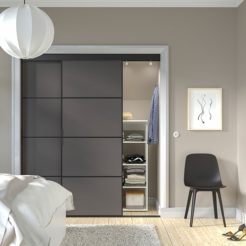 Dormitorio moderno con armario SKYTTA gris, ropa cuidada, silla negra, luz blanca, cama y arte de pared.