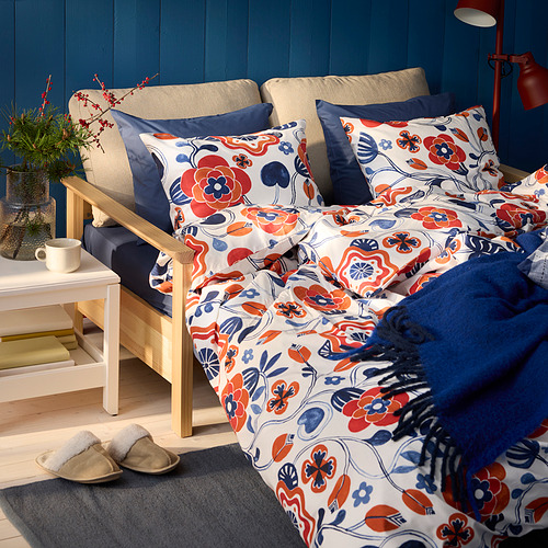 Ropa de cama KANONVISKA con estampados florales en rojo, azul, blanco. Mezcla de algodón, transpirable, sobre sofá cama beige. Espacio acogedor y bien decorado.