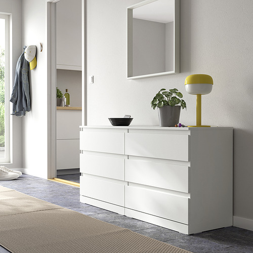 Cómoda blanca LILLBERGET de seis cajones con diseño elegante, espejo, lámpara, planta, cuenco y chaqueta.