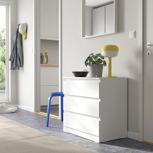 Lámpara LILLBERGET amarillo brillante en una cómoda blanca con cajones, junto a la silla azul, cerca de la entrada con gancho y puerta.