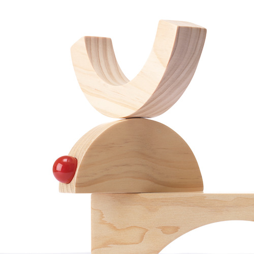 Juguete de equilibrio de madera sobre fondo blanco, con madera lisa de color claro y una sola cuenta roja, que muestra artesanía de alta calidad.