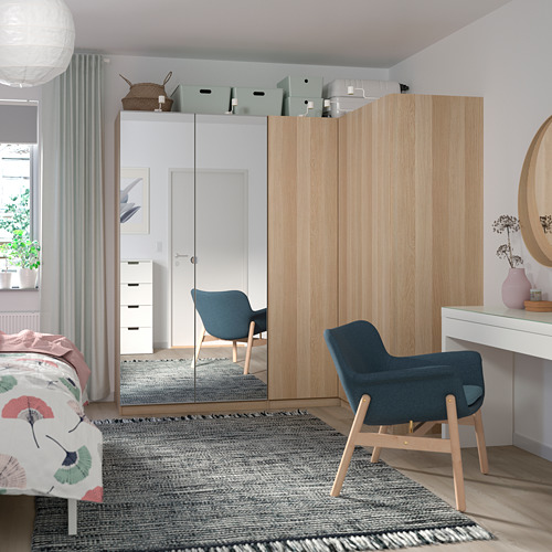 Un dormitorio moderno, un armario de madera clara FORSAND, una silla azul y un escritorio con cortinas transparentes que permiten la entrada de una luz suave.