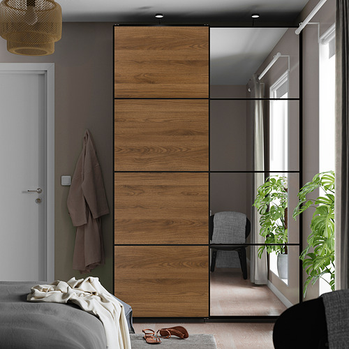 Dormitorio con armario de puertas correderas AULI con paneles de madera y espejos, colocado junto a una cama con ropa y sandalias.