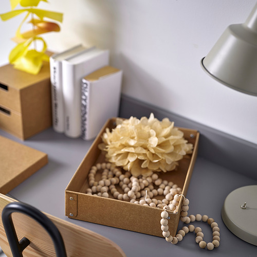 Expositor en caja con cuentas de madera y flores secas sobre el escritorio, junto a libros y lámpara.