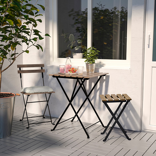 Pequeño montaje exterior con mesa, silla y taburete plegables TÄRNÖ en madera natural y metal negro. Perfecto para espacios compactos, rodeados de plantas.