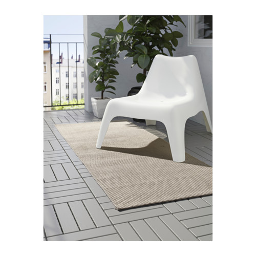 Balcón moderno con silla geométrica blanca, alfombra exterior beige y planta en maceta.