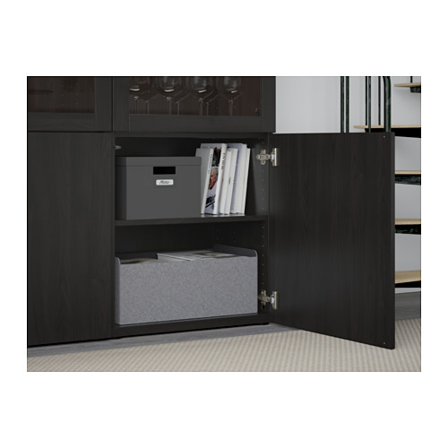 Un armario BESTÅ negro con una puerta abierta, con estantes ajustables que contienen cajas de almacenamiento grises y libros.