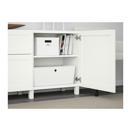 Mueble de almacenamiento BESTÅ blanco con estantes y cajones, una puerta abierta que revela cajas de almacenamiento y libros.