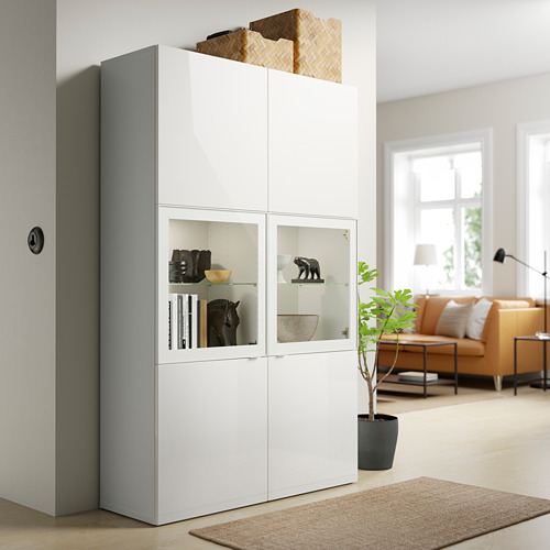 Mueble SELSVIKEN blanco con puertas y decoración de cristal, junto a una ventana y sofá naranja.