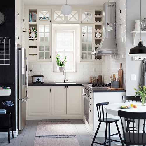 Cocina moderna con gabinetes blancos, sillas negras, electrodomésticos de acero inoxidable y una alfombra.