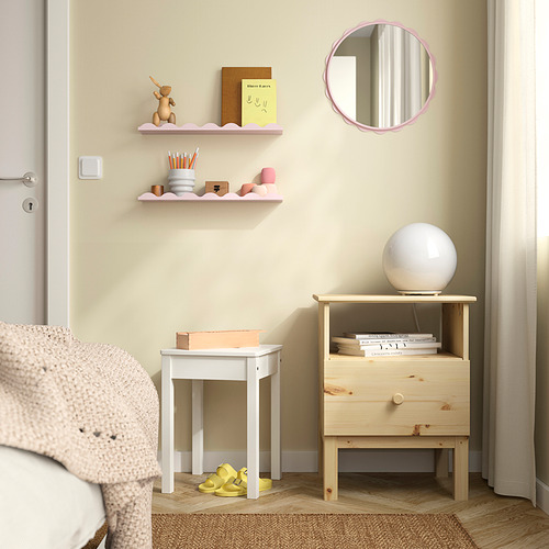 Rincón acogedor: espejo rosa suave sobre mesita de noche de madera, lámpara, libros, manta rosa, zapato amarillo solitario.