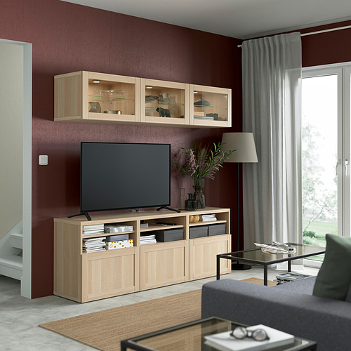 Gran sala de estar moderna con paredes rojas, con mueble de TV y gabinete de vidrio de roble claro SINDVIK, sofá gris, mesa de café y televisor de pantalla plana grande.