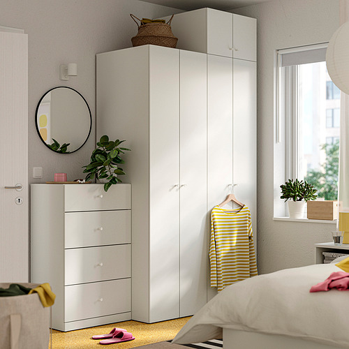 Dormitorio moderno con muebles LASTARE blancos. Armario, cofre, espejo, planta, camisa amarilla, cama, zapatillas rosas.