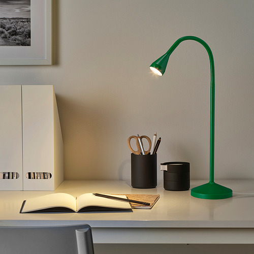 Pequeña lámpara de escritorio verde NÄVLINGE sobre una mesa con cuaderno y papelería, que proporciona luz enfocada y se integra en la decoración.