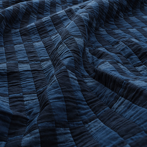 Manta acolchada azul oscuro con costuras visibles, detalle de textura doblada.