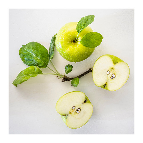 Imagen manzanas verdes: una entera, dos mitades, mostradas sobre una superficie blanca. Hojas adheridas, mostrando el estado natural de los frutos.