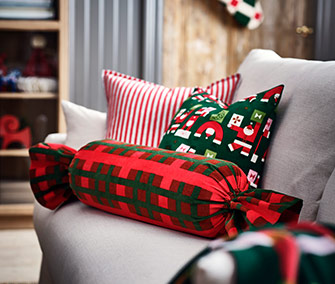 Cojines de Navidad sobre un sofá beige. Incluye uno en forma de caramelo a cuadros rojo/verde, otro a rayas y uno verde con figuras.