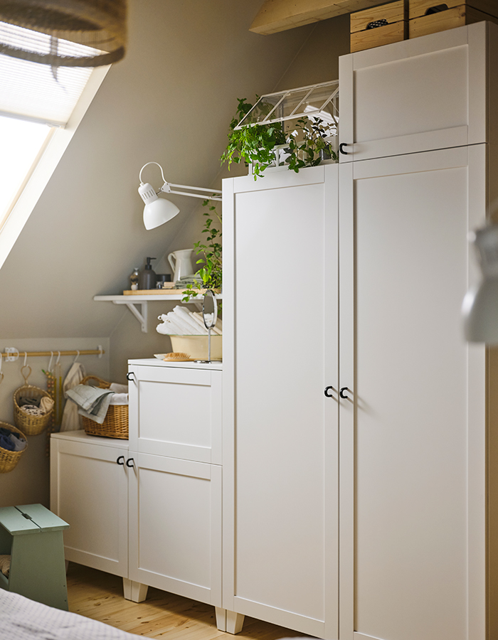 Sloped ceiling space with white storage furniture, decorative plants, and hanging baskets; bright and natural atmosphere.