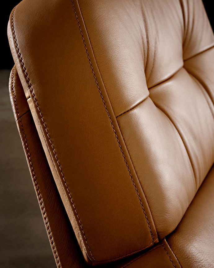Close-up of a camel-colored leather armchair backrest, showing detailed double stitching and the soft, cushioned texture of the hide.