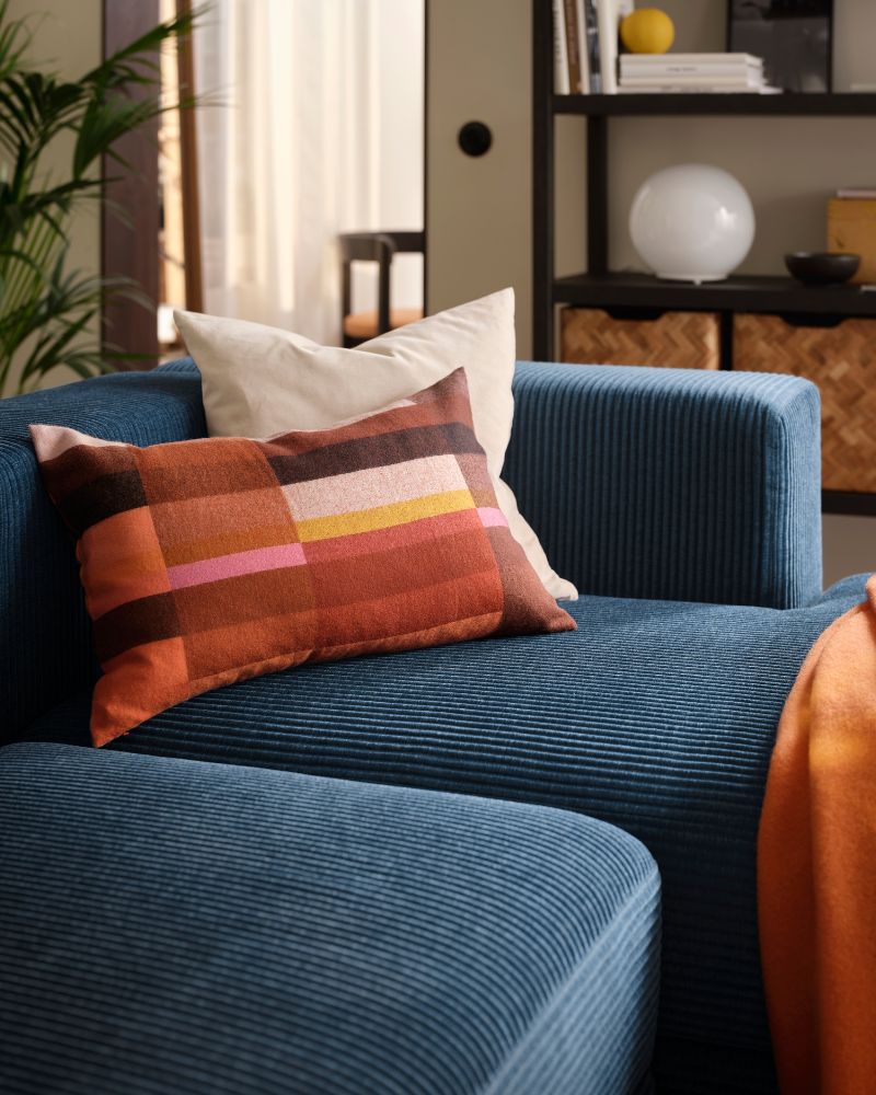A living room with a dark-blue JÄTTEBO four-seat modular sofa with a chaise longue, holding a pair of cushions and a throw.
