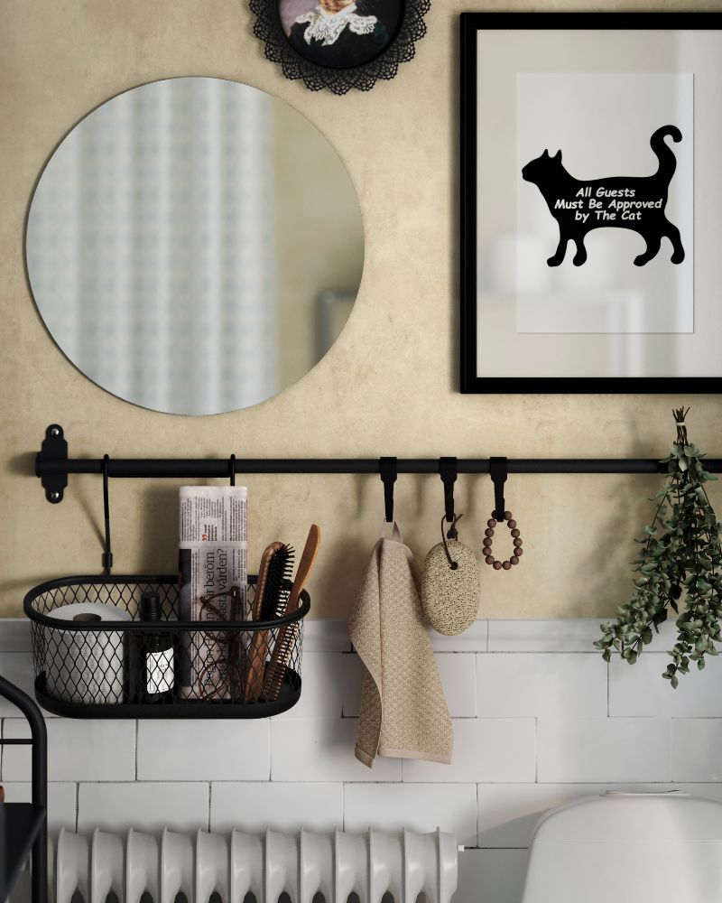 A black metal HULTARP rail is above a toilet and has a wire basket with a newspaper, eyeglasses and a roll of toilet paper.