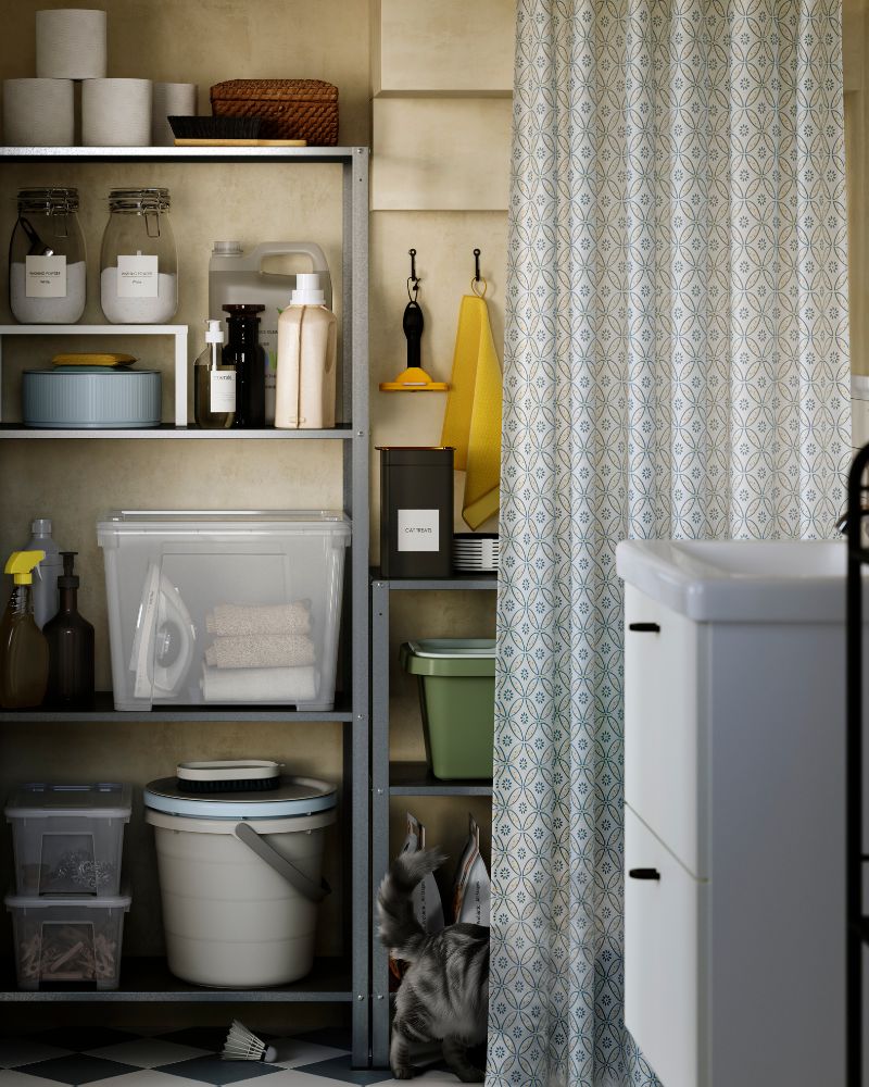 A galvanised steel HYLLIS in/outdoor shelving unit holds cleaning supplies and toilet paper rolls in a small bathroom.