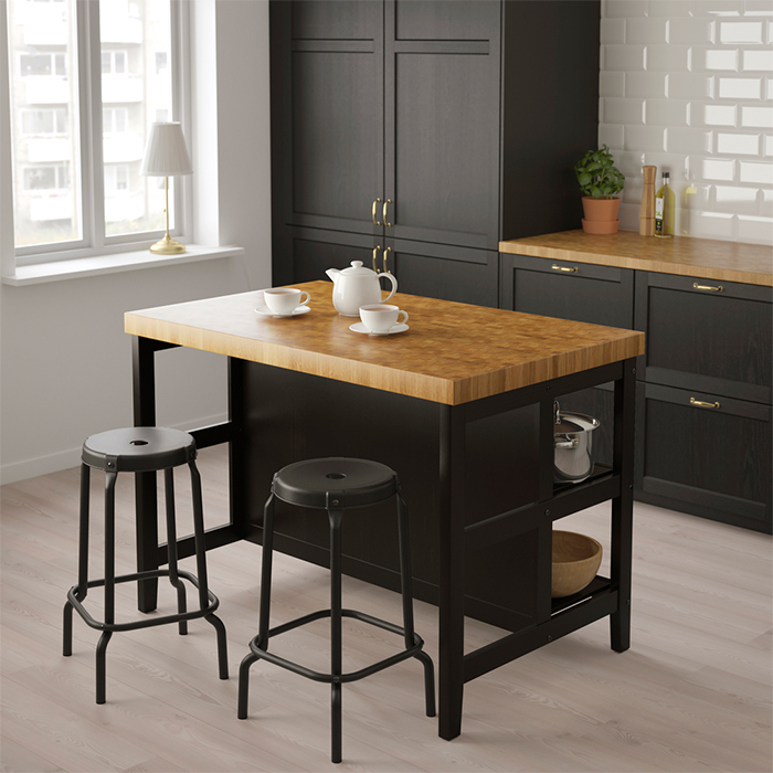 Cocina de estilo tradicional con isla central de base negra y encimera de madera tipo roble, dos taburetes altos y un juego de té sobre la isla.