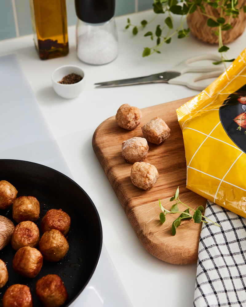 Albóndigas de pollo HUVUDROLL de IKEA sobre un sartén y una tabla de madera.