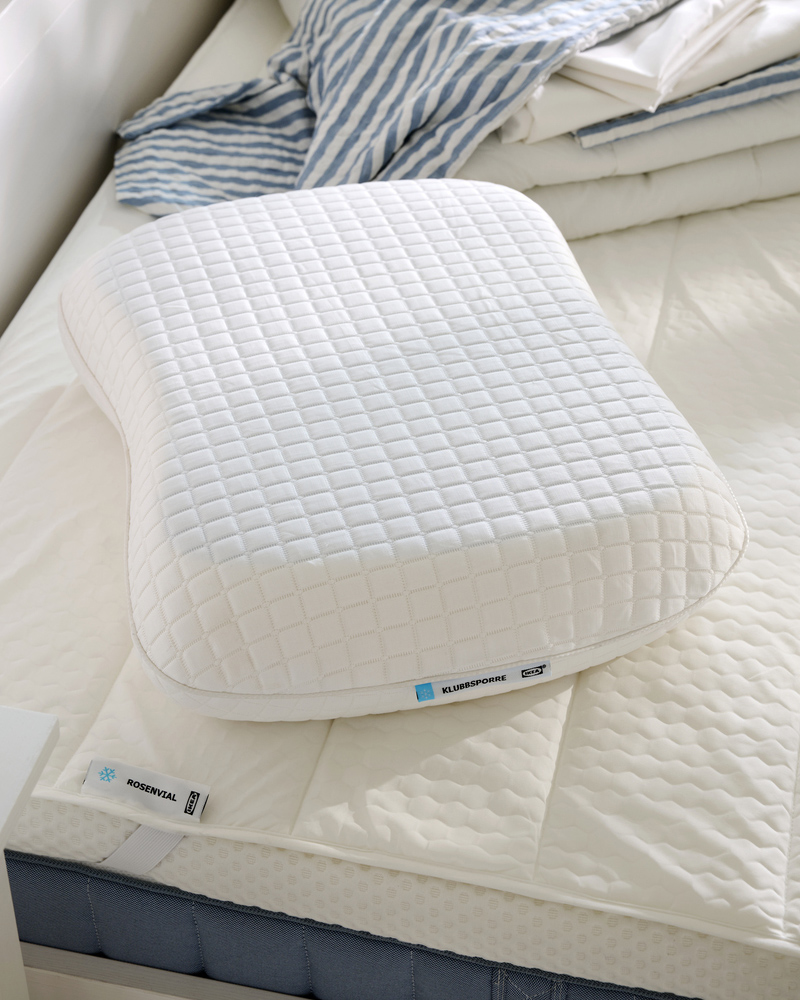 Primer plano de la almohada ergonómica KLUBBSPORRE sobre el protector de colchón ROSENVIAL, ambos en material refrescante.