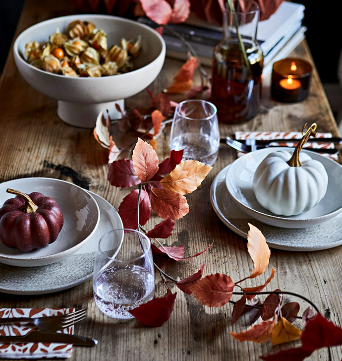 Mesa otoñal con calabazas decorativas, hojas secas y vajilla rústica.
