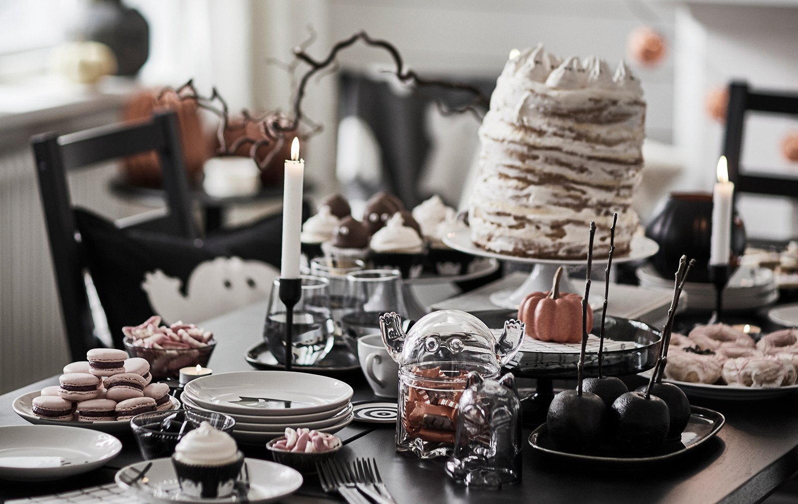 A dark table with KUSTFYR side tables, several treats, a KUSTFYR bowl with lid shaped like a ghost and some lit candles.